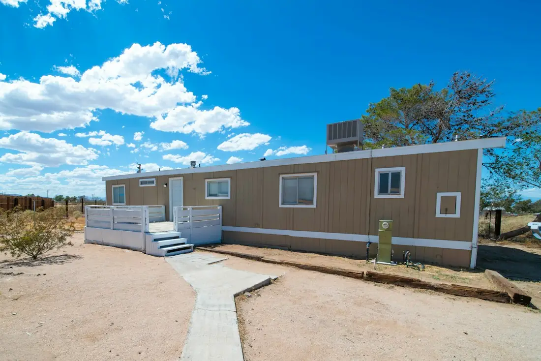 A single-wide manufactured home with a small front deck under a blue sky